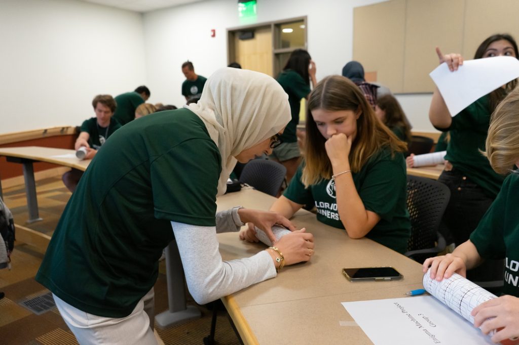 Student assists cybersecurity camp participant with enigma machine