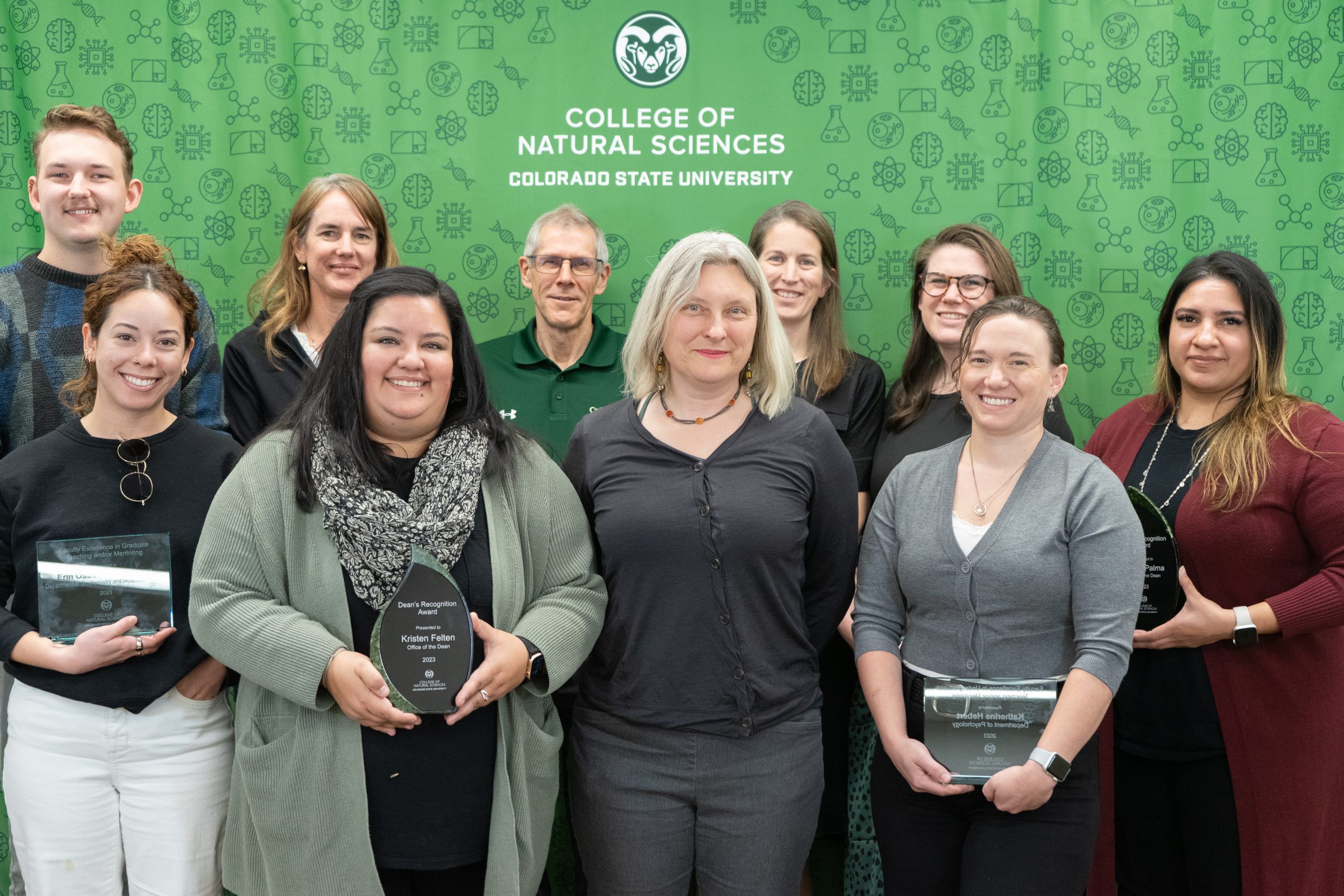 A group of 2023 award winners in front of a green C S U backdrop, many holding awards.