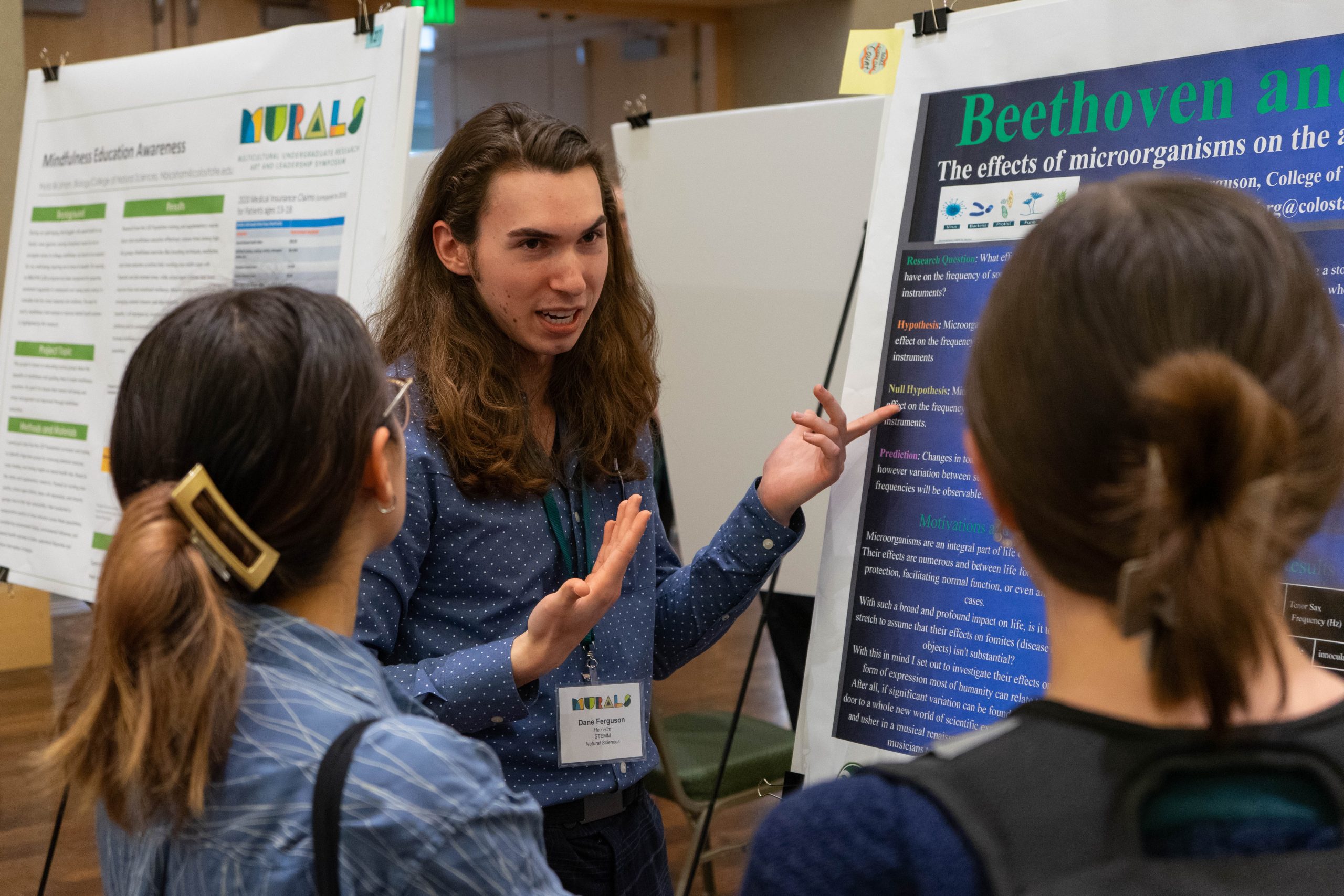 A student explains their research poster to a group of onlookers. 