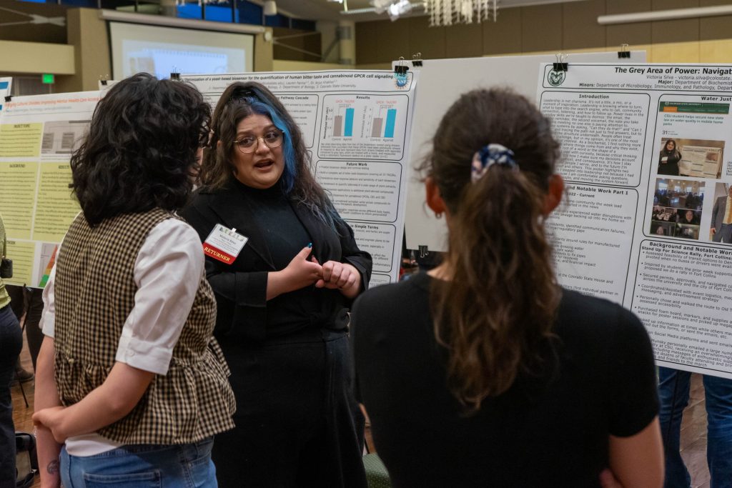 A student explains their research poster to two onlookers.