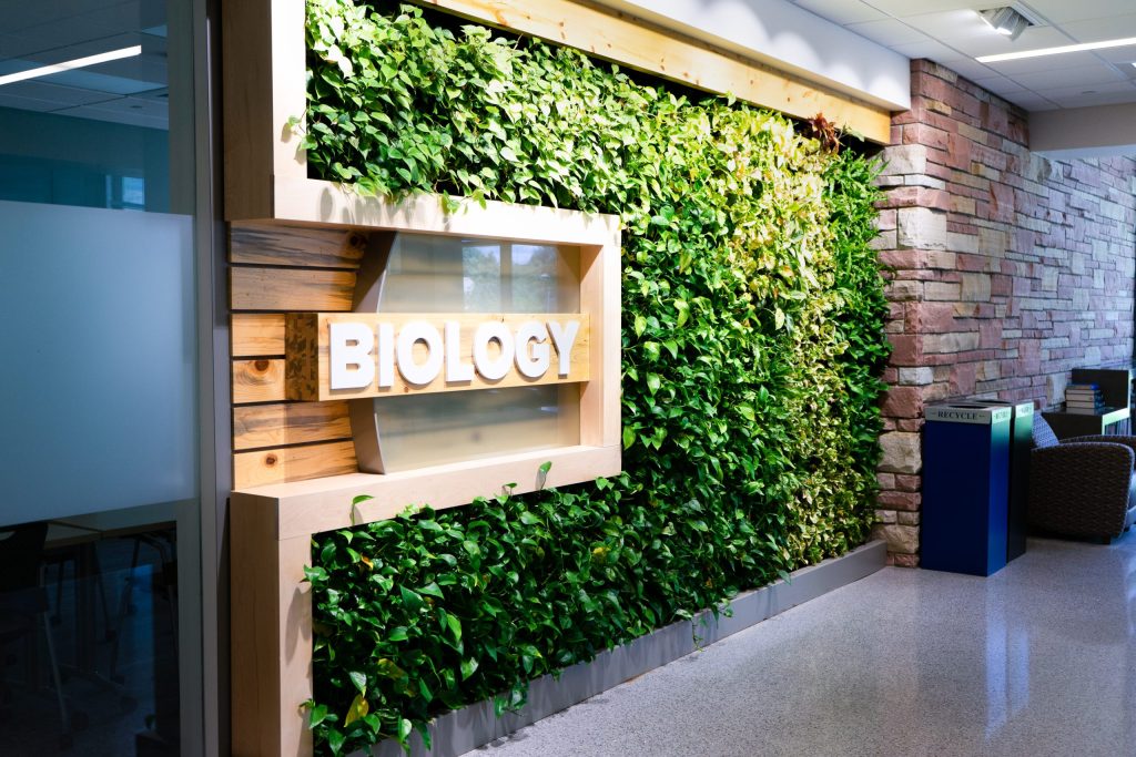 Plants grow out of the wall near a sign that reads "Biology."