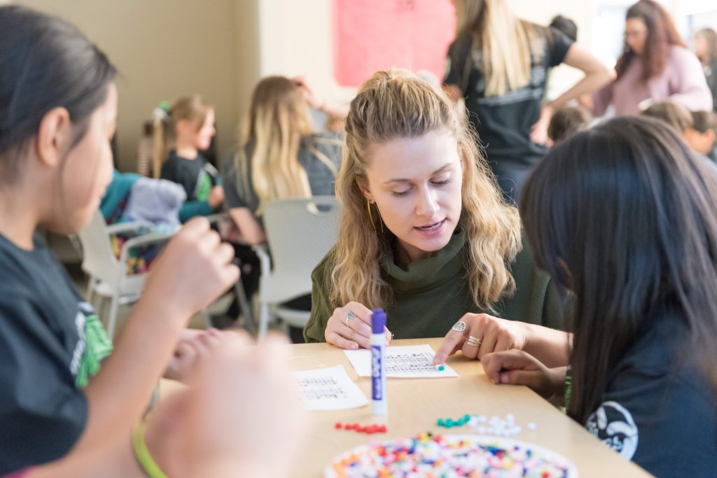 A college-aged student walks two younger students through a science activity.